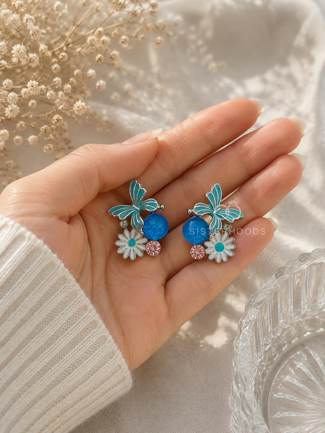 Blue butterfly and daisy stud earrings with white and pink floral accents | SISTERHOODS-SHA256:cc1d0dda62d491f592521f78bef324a7aa9e00571d5eb17fe1b4b2ae3374b6b3