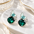 Teal butterfly dangle earrings with faceted green oval accents and white details | SISTERHOODS-SHA256:ce7de57a8b6e01689edfe65c2d6075fe98a885a4cdf11de74e4faca7cae16541