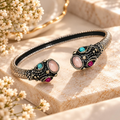 Ornate open cuff bracelet with dark detailing and pink and turquoise oval accents | SISTERHOODS-SHA256:7666625003b3a00222bd32efd219ebc4f318dd9814d72c05412260e72ecbd1f8