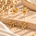 Gold-coloured floral stud earrings with long bow-shaped dangling charms | SISTERHOODS-SHA256:9e8ae984779f19ccd4d4af5fc7320eadd544d8ed2eebef016df2f0465a09c7f3