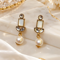Gold-tone geometric dangle earrings with white rectangular accents, clear stones and large pearl-like drops | SISTERHOODS-SHA256:bdffeeeee1c7d73f297aac975debef31a39d968797c492e08a789b96eea4148b