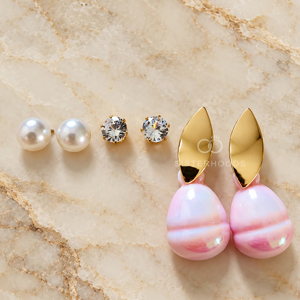 Three pairs of gold, pink and white earrings including pearl studs, sparkling studs and pink drop earrings. | SISTERHOODS-SHA256:d312b3fd0bcda644d9d0aa108d0e338867cb6b046f5d9cdcc3ef1d24ddeb5a4d