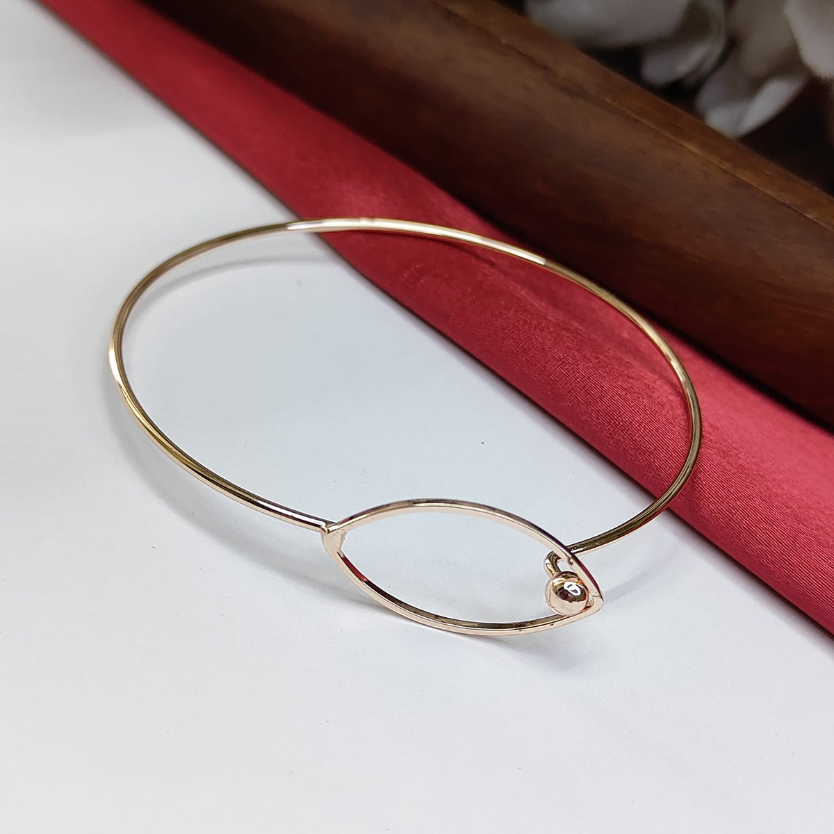 Gold bracelet on a white surface with a red fabric background