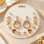 Gold-tone multi-style earring set with studs, bow drops, floral accents and heart-shaped designs | SISTERHOODS-SHA256:e4e93f4702cfcc61b3114166cacf6bb1adf001b3b70040a3251596e538a48c38