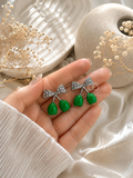 Silver bow-shaped dangle earrings with glossy green drop accents | SISTERHOODS-SHA256:e199773fa9dc2155dca640fac7aaa77acbf72a05421dc78a57538d4b8fdc0307