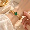 Gold-tone open bracelet featuring a green clover centre and floral cutout details | SISTERHOODS-SHA256:c10db9d1445762b24b616643595b583a889d91f4b2a46d96669c30ed60ecccc6