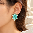 Aqua and cream flower stud earring with gold-tone detailing worn on an ear | SISTERHOODS-SHA256:4a637c0fde22ee7bf054c471ed89bebf175c29d8dac7e2fa38b13090aeeb218b