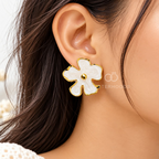 White blossom-shaped gold-tone stud earring worn on an ear | SISTERHOODS-SHA256:4871f247b650aa4756377d8c538ef307b06d741202757feeab30bd9a89465fc5