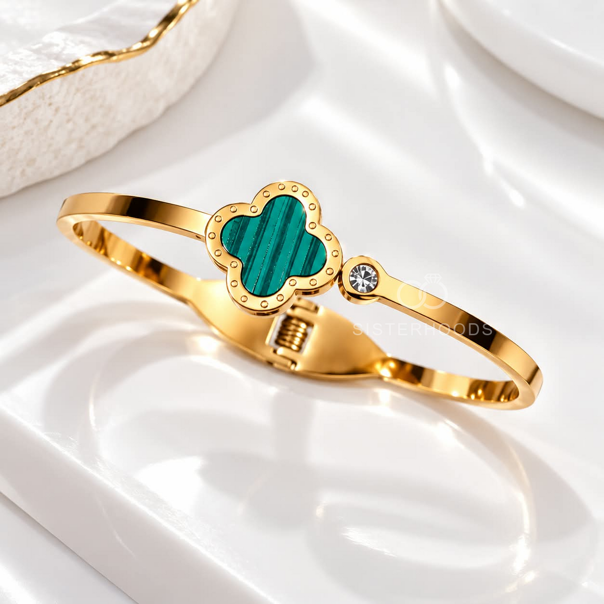 Gold-tone cuff bracelet with a teal quatrefoil centre and small accent detail | SISTERHOODS-SHA256:398dbb733c8ed0b139245cff35869b17177b79888b234a170443a902fe63155c