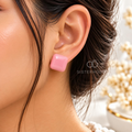 Pink square stud earring worn on an ear | SISTERHOODS-SHA256:0af19de3abf42d02af4d2f16389975ad362668f81295cedc917b0a00aeddc8f5