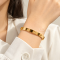 Golden cuff bracelet with repeating circular screw motifs worn on a wrist | SISTERHOODS-SHA256:2847ad799ab427335ea3a00eeaec3e3dd53c99e6dfb761c6971d93c3b5c68993