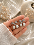 Silver bow earrings with white dangling drops | SISTERHOODS-SHA256:c3c9ee3bf0aa55f2210e46d360249cd80849c2d1323029b48cf0c370aaaa8915
